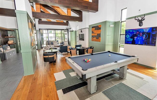 Community room with billiards table, tables with chairs, and a lounge with wooden beams above