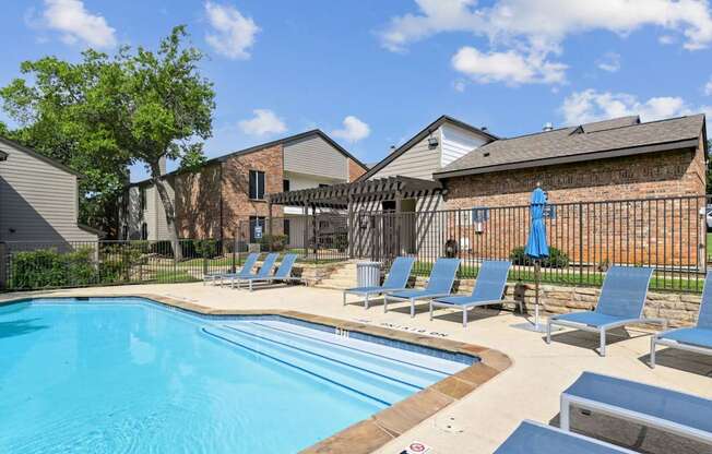 A swimming pool surrounded by lounge chairs and a fence at The Oaks of Denton Apartments in Denton, TX