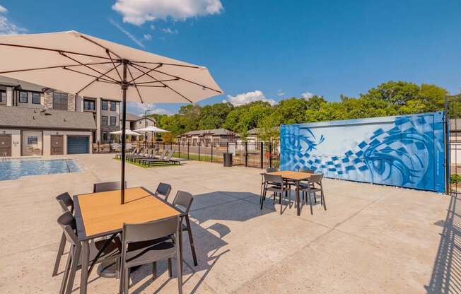 A table with chairs and an umbrella is in the foreground of a patio area.at Evolve at Parkway Apartment Homes, Concord