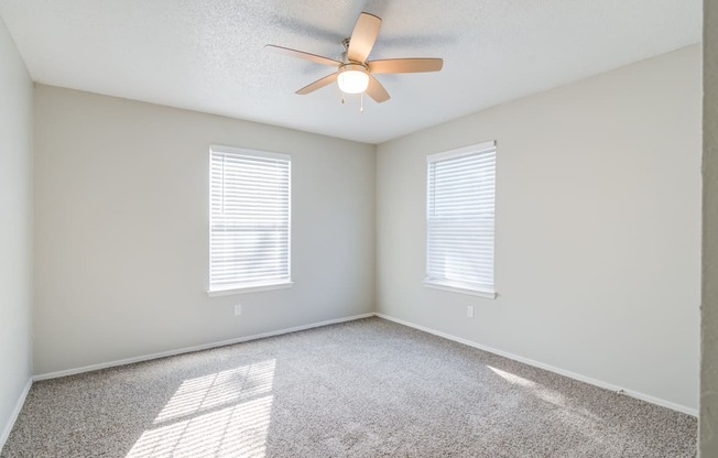 A room with a ceiling fan and two windows.