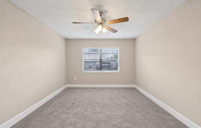 A room with a ceiling fan and a window with blinds.