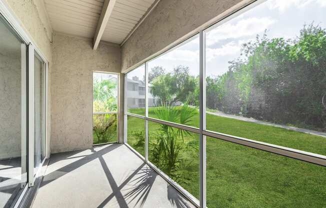 a screened in porch with a view of a grassy area and a building in the background
