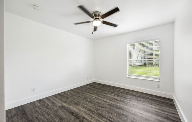 an empty living room with a ceiling fan and a window