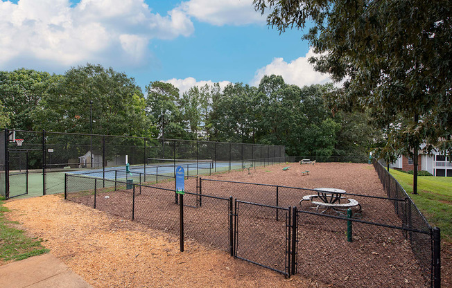 A tennis court surrounded by a black fence with a blue sign in the middle.