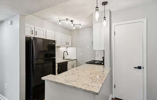 A kitchen with a granite countertop and a black refrigerator.