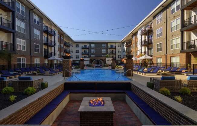A pool surrounded by a brick patio and a fire pit.