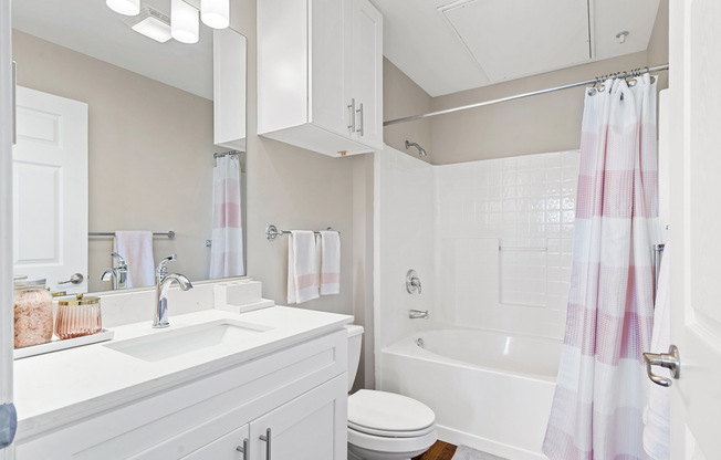 Updated bathroom at Kelly’s Ridge Apartments in Columbia, MO, featuring a white vanity with quartz countertop, chrome fixtures, overhead and under-sink storage, a curved shower rod create a clean, spa-like feel.