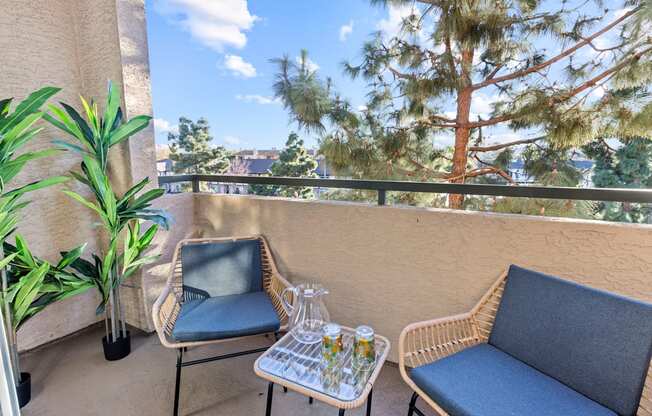 A balcony with a chair, a sofa, and a table with glasses and a pitcher on it.
