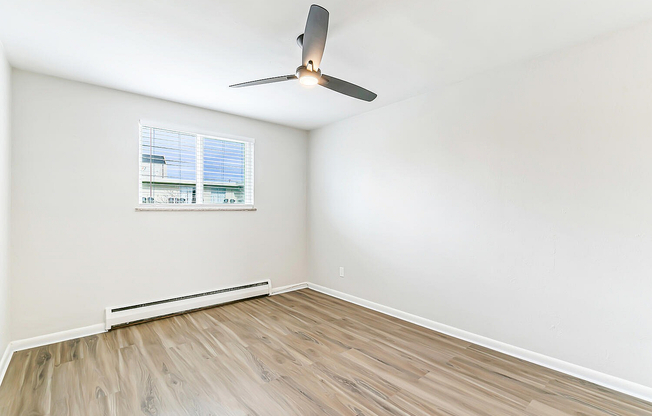 Bright, spacious room with elegant wood flooring, large window for natural light, and modern ceiling fan.