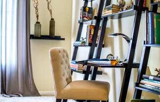 A chair is in front of a bookshelf with a glass of beer on the table.