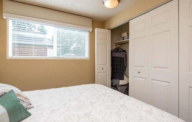 A bedroom with a bed, a window with blinds, and a closet.