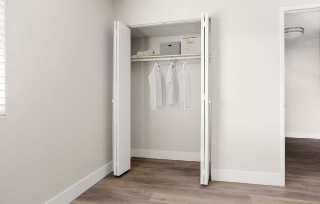 a walk in closet in a bedroom with white walls and a wooden floor