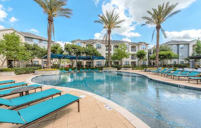 A swimming pool surrounded by sun loungers and palm trees.