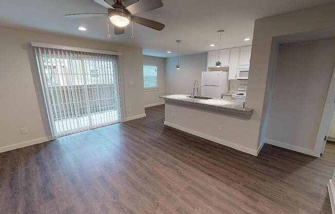 A spacious kitchen and living room with hardwood floors and a ceiling fan.