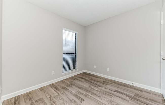 A room with wooden flooring and a window with blinds.