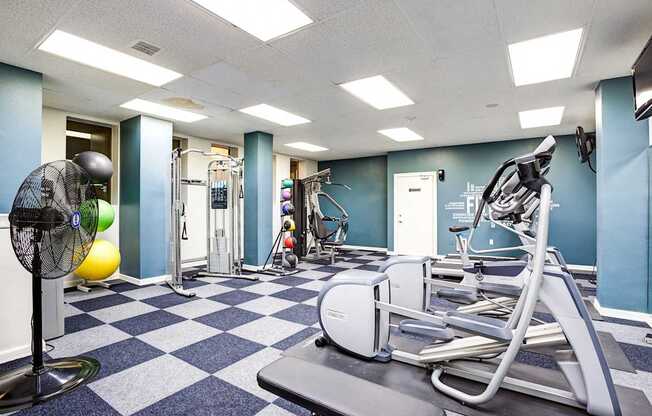 A gym with a fan, weights, and exercise equipment.