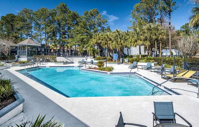 A swimming pool surrounded by trees and chairs.