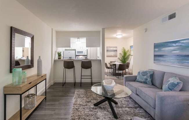 A modern living room with a grey sofa and a glass coffee table in the 558 square foot 1 bedroom, 1 bath model apartment at The Summit at Midtown Apartments in the Dallas Midtown neighborhood of Dallas, TX.