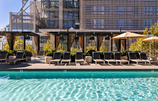 A pool area with lounge chairs and umbrellas in front of a large building.