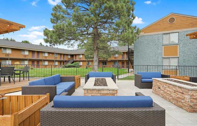 A large tree is in the middle of a patio with blue couches and wooden tables at Mountain Vista Apartments, Lakewood, CO