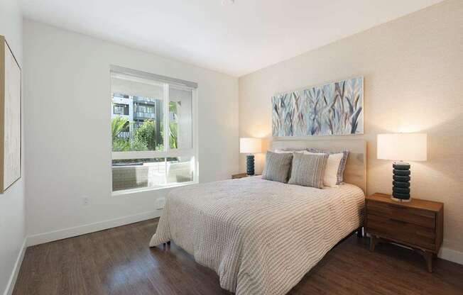 A bedroom with a bed, nightstand, and a painting on the wall.