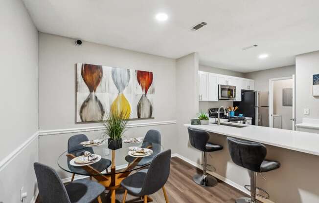A dining room with a table set for six and a painting on the wall.