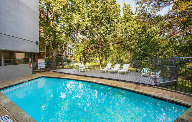 a swimming pool with chairs and a building in the background