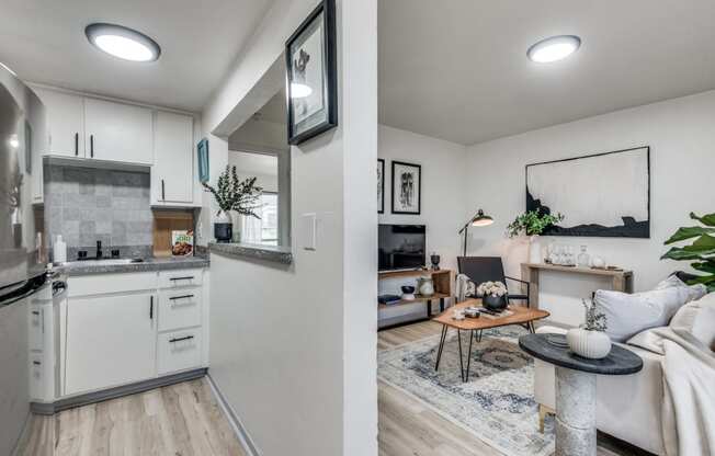 a kitchen and living room with white cabinetry and hardwood floors