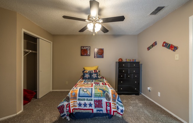 A bedroom with a bed, dresser, and ceiling fan.