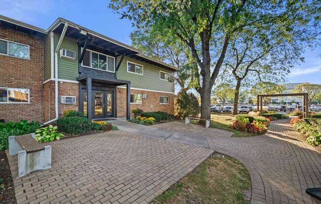 a brick and green building with a walkway and trees