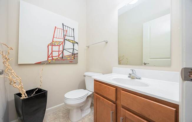 A bathroom with a toilet, sink, and a painting of a chair.