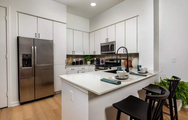 A kitchen with a white counter and black chairs.