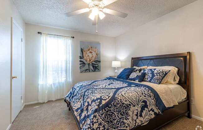A bedroom with a bed, a ceiling fan, and a painting on the wall.