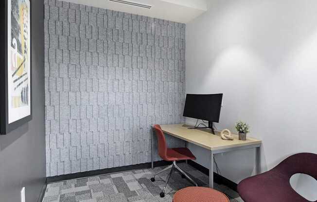 A small office with a desk, chair, and trash can.