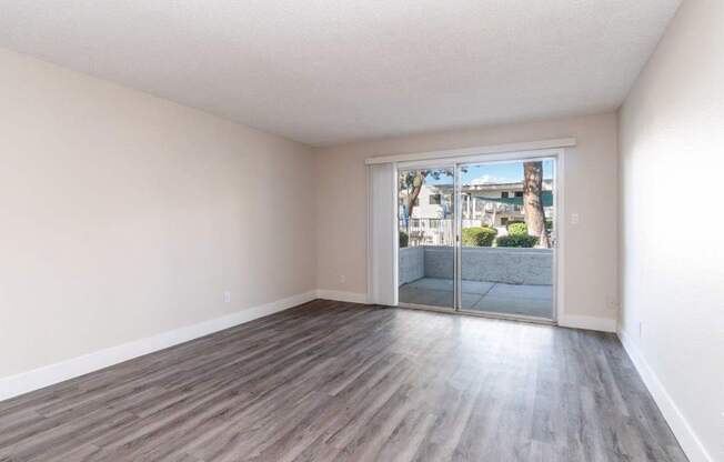 A room with wooden flooring and a sliding glass door leading to a balcony.