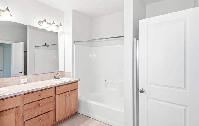 A white bathroom with a sink, mirror, and bathtub at The Landing Apartments and Townhomes, Oregon, 97045
