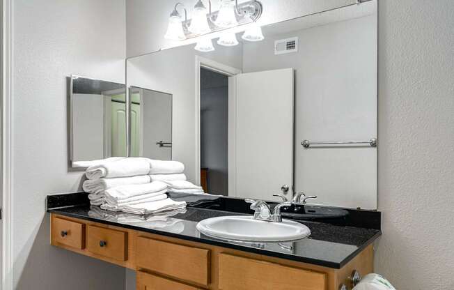 A bathroom with a sink, mirror, and towel stack.
