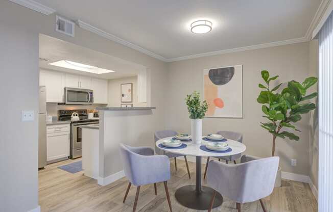 Two-Bedroom Apartments in Moreno Valley, CA - Ardella on Chagall - Dining Area with Hardwood-Style Flooring, Round Table and Four Chairs, Houseplant, and View of Kitchen.