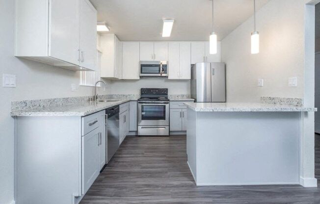 Alternate view of kitchen with stone counters, white cabinets, stainless appliances