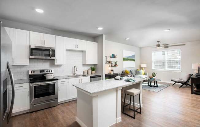 a kitchen and living room with white cabinets and stainless steel appliances at 55 Fifty at Northwest Crossing, Houston Texas