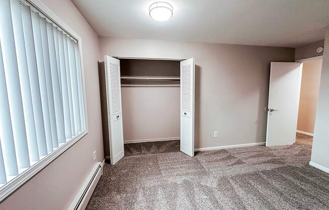 A room with a carpeted floor and a window with blinds.