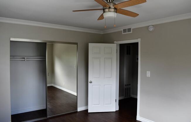 View of bedroom with wood look flooring, sliding glass mirror closet, and ceiling fan