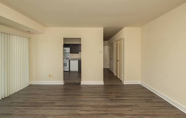 A room with wooden floors and a kitchen area in the background.