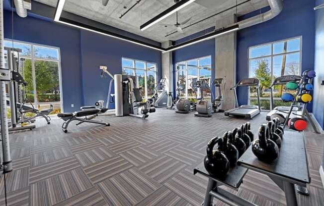 a gym with weights and other exercise equipment in a building with large windows