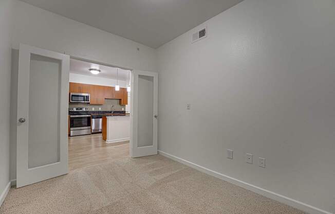 A room with a carpeted floor and a kitchen visible through the open door. at Vue Greenville, Dallas, 75206