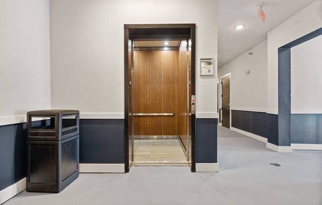 A hallway with a wooden door and a trash can.