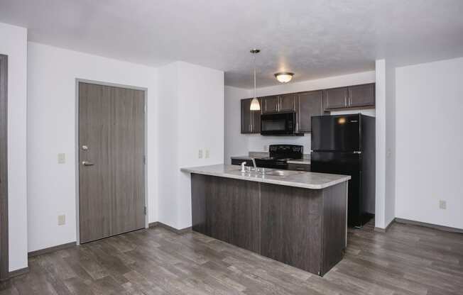 an empty living room with a kitchen with a refrigerator and a sink