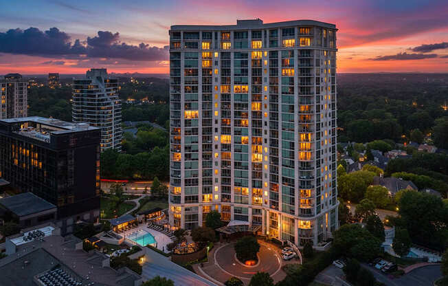 A tall building with a pool in front of it is lit up at dusk.