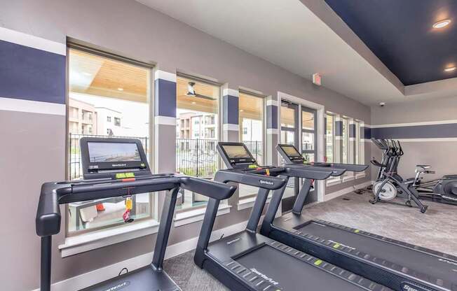 A treadmill in a gym with a view of a balcony outside.