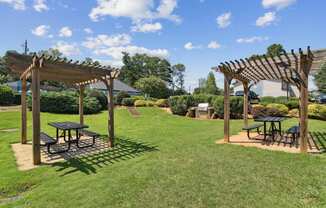A sunny day at a park with picnic tables and pergolas.